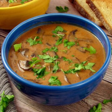 Vegan Hungarian Mushroom Soup, served in a blue bowl with fresh parsley scattered on top.