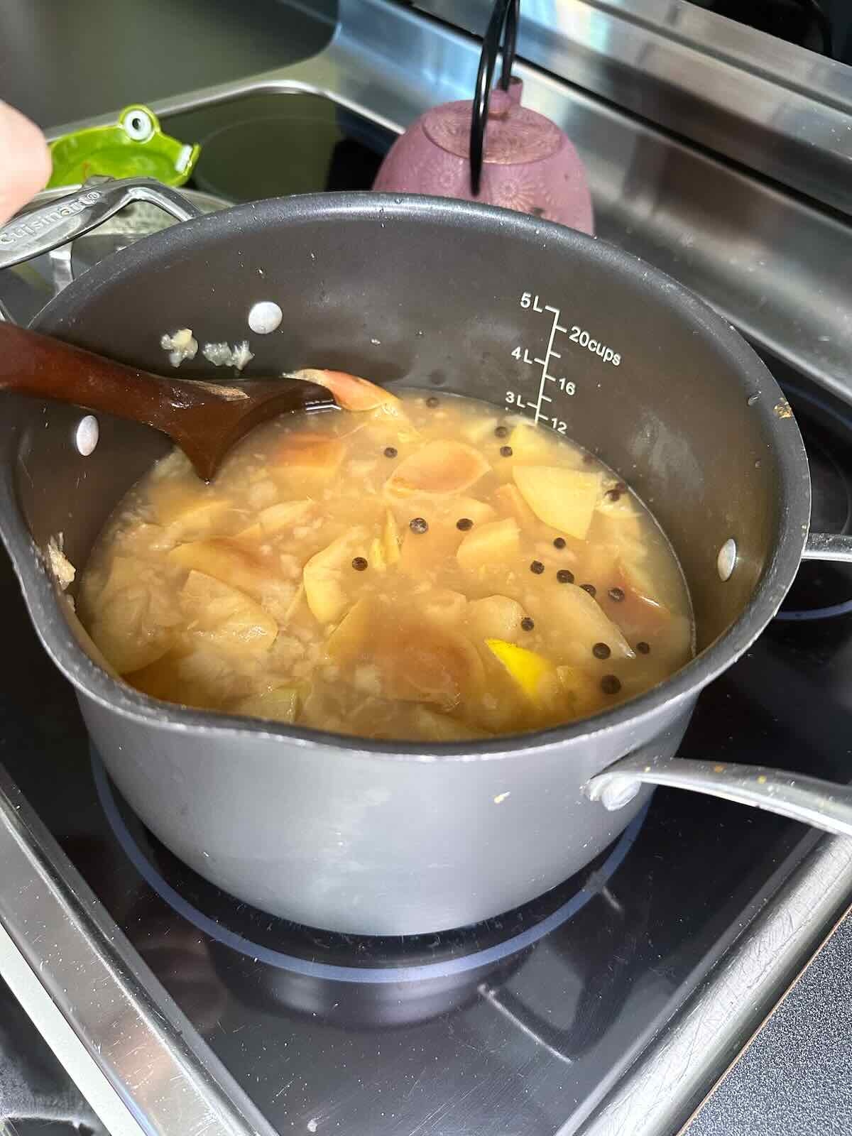 Mashing softened apples with a wooden spoon in a pot while making Spiced Apple Cider.