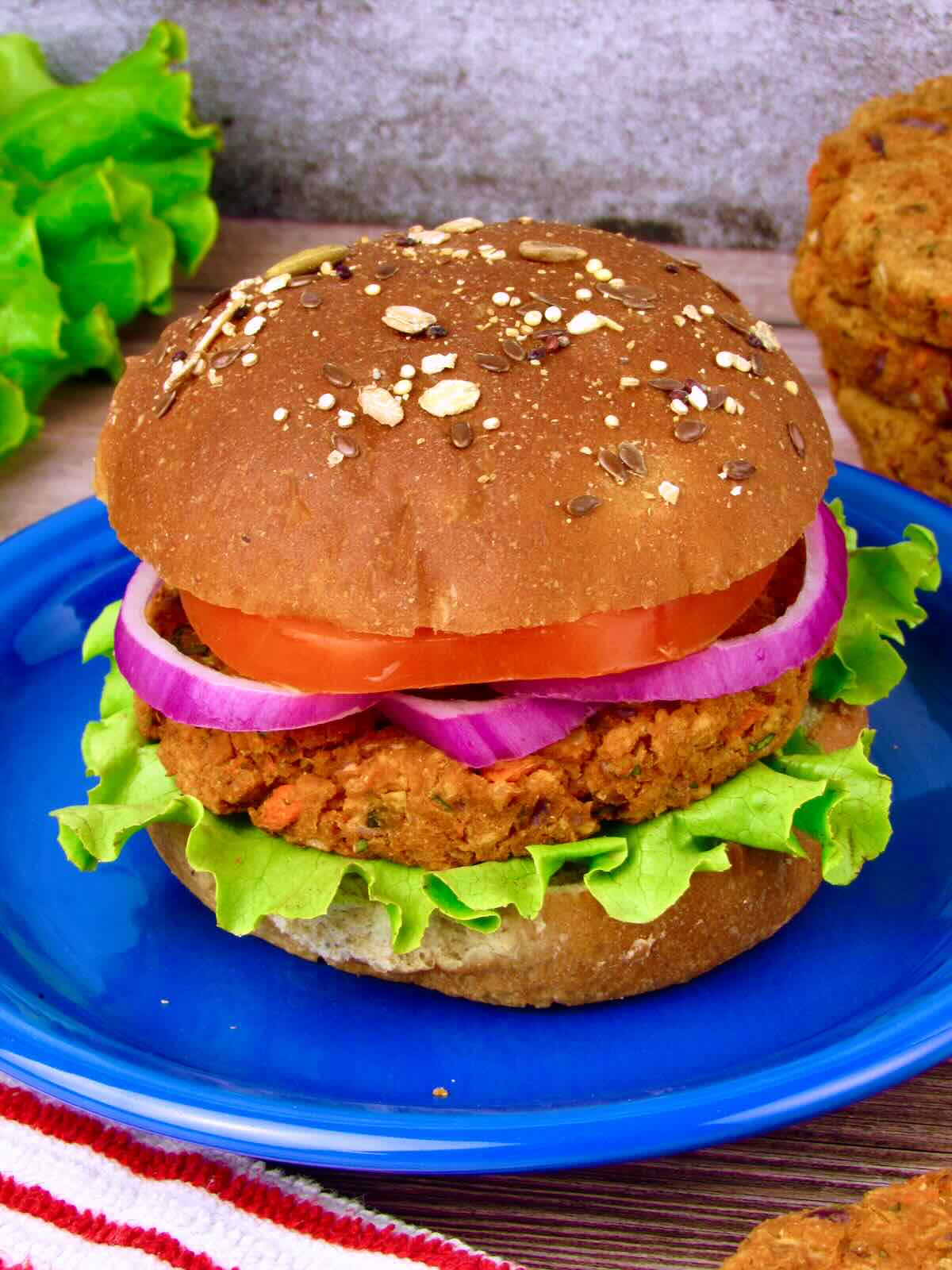 Chickpea Veggie Burger on a whole grain bun topped with lettuce, tomato, and red onion, served on a blue plate.