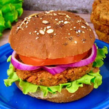 Chickpea veggie burger on a whole grain bun with lettuce, tomato, and red onion, served on a blue plate.