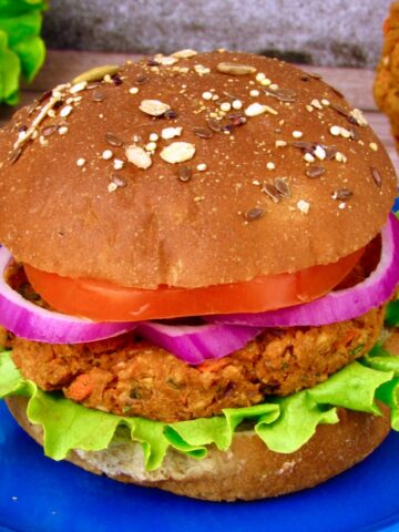 Chickpea veggie burger on a whole grain bun with lettuce, tomato, and red onion, served on a blue plate.