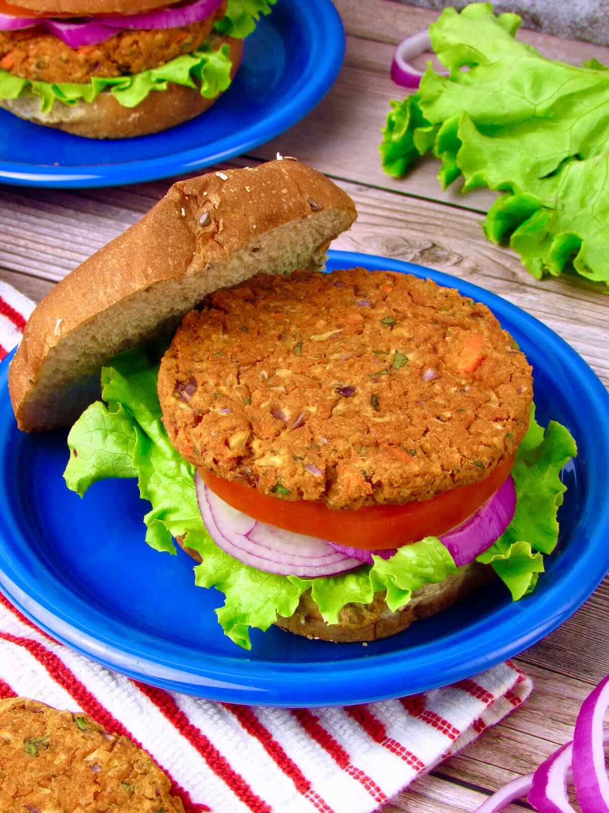 Homemade Chickpea Veggie Burger with lettuce, tomato, and red onion on a whole grain bun, top bun tilted to show patty texture.
