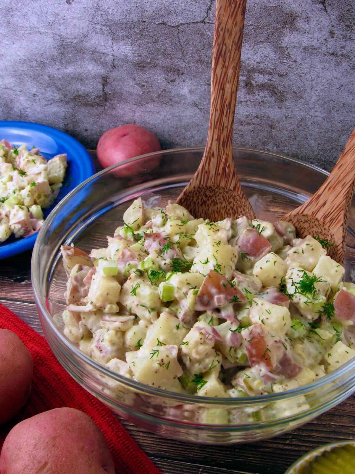 Bowl of Vegan Potato Salad with red potatoes, celery, and fresh dill, served with wooden salad spoons.