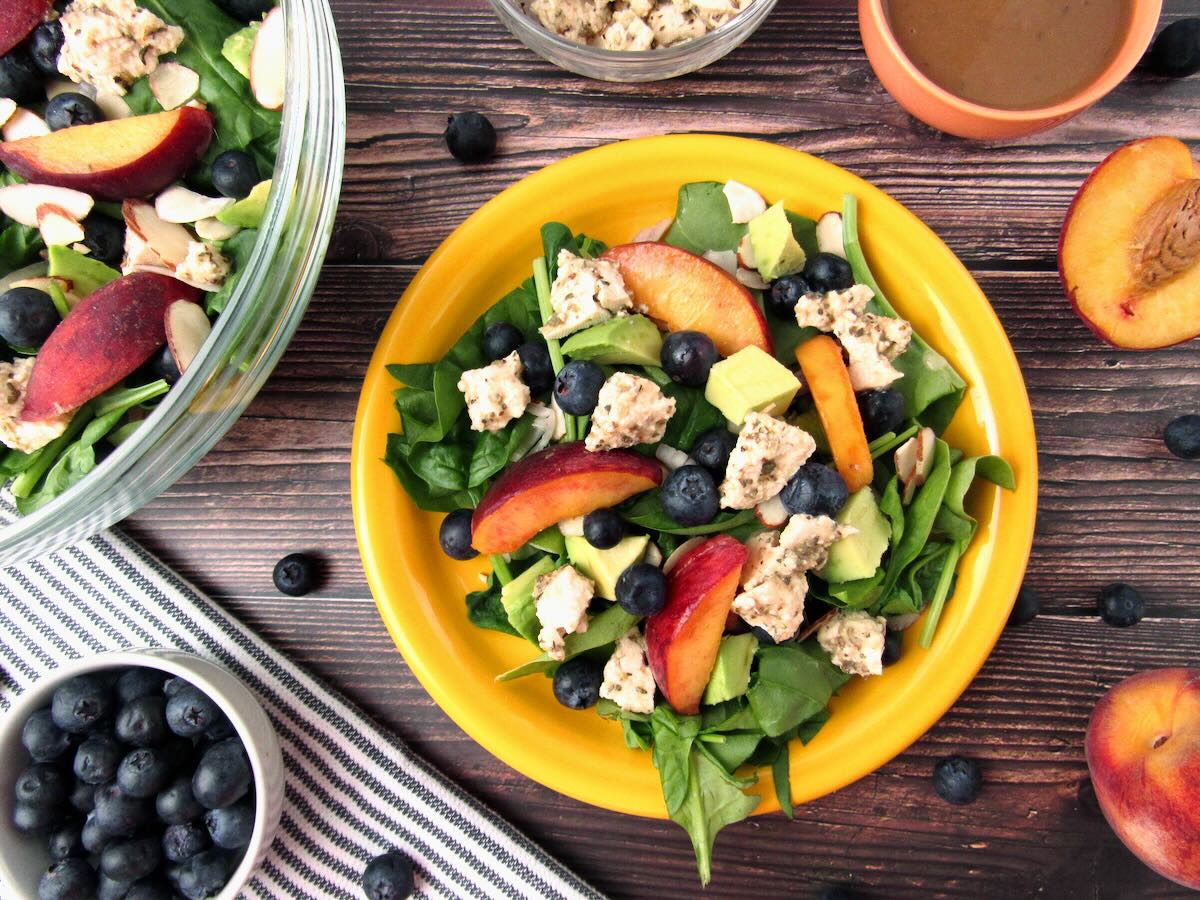 Overhead view of Peach Summer Salad on a yellow plate with peaches, blueberries, vegan feta, and balsamic dressing nearby.