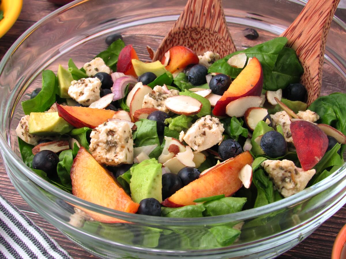 Close-up of a vibrant Peach Blueberry Salad featuring juicy peach slices, plump blueberries, creamy avocado, tangy vegan feta, spinach leaves, and crunchy almonds.