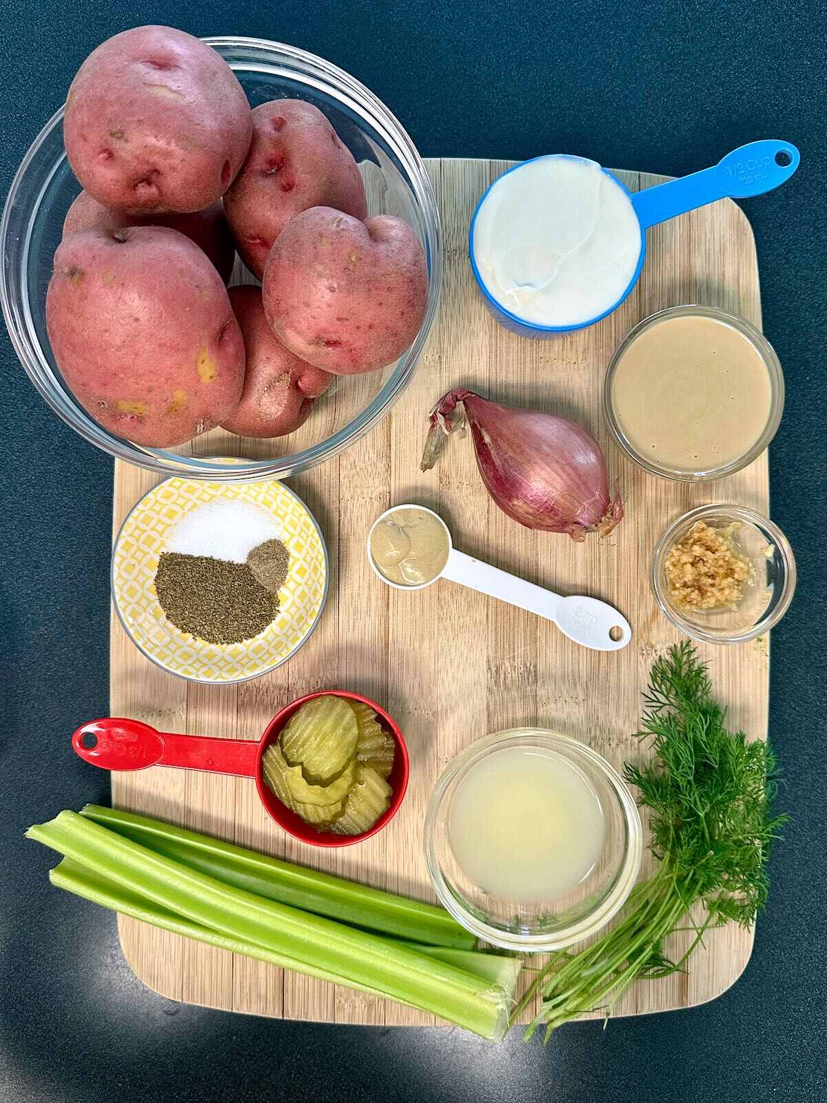Overhead view of ingredients for Creamy Vegan Potato Salad, including red potatoes, celery, pickles, dill, and vegan mayo.