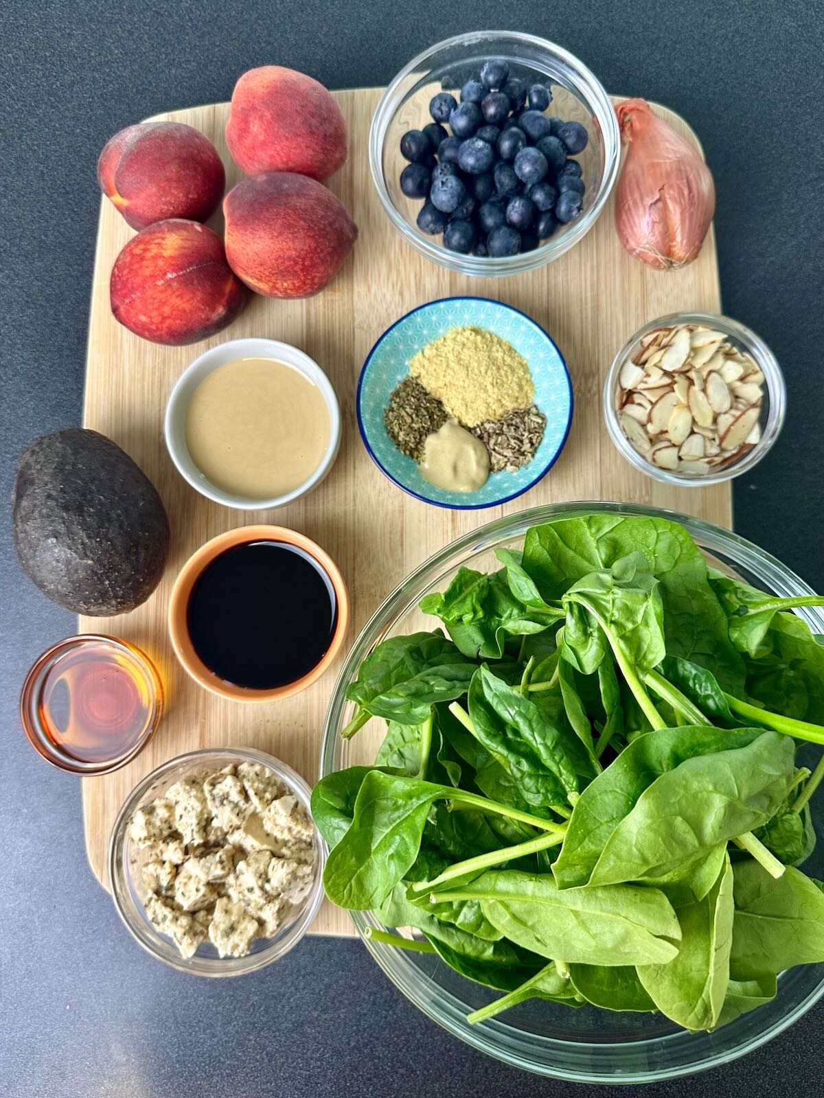 Overhead view of salad ingredients and oil-free balsamic dressing components, including peaches, blueberries, avocado, vegan feta, spinach, almonds, shallots, and dressing ingredients.