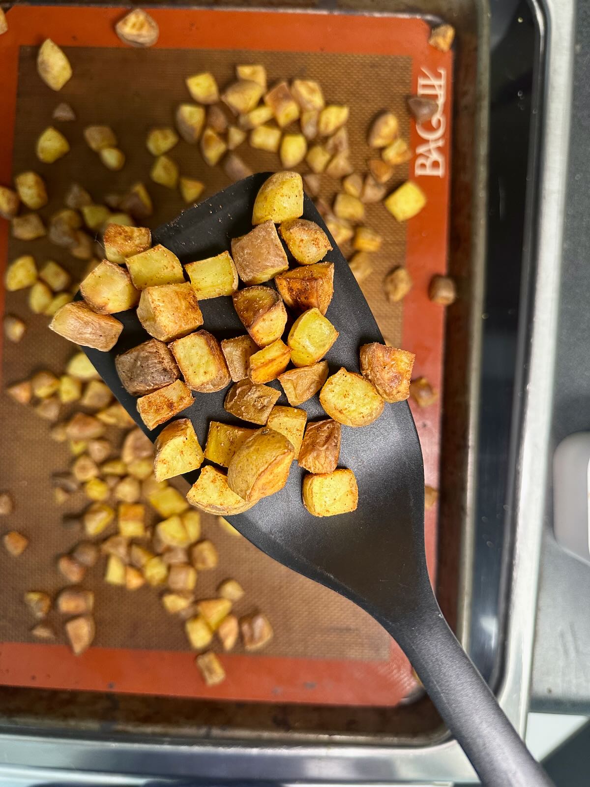 Spatula lifting oil-free oven roasted potatoes from a pan for Vegan Breakfast Burritos.