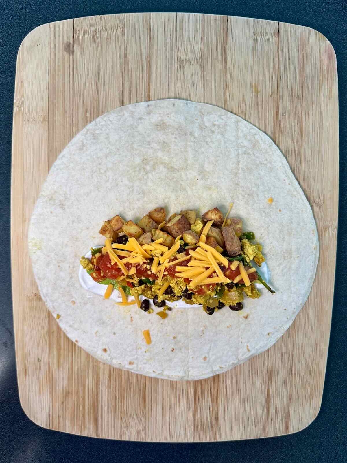 Flour tortilla filled with tofu scramble, roasted potatoes, and vegan cheddar cheese before rolling into a Breakfast Burrito.