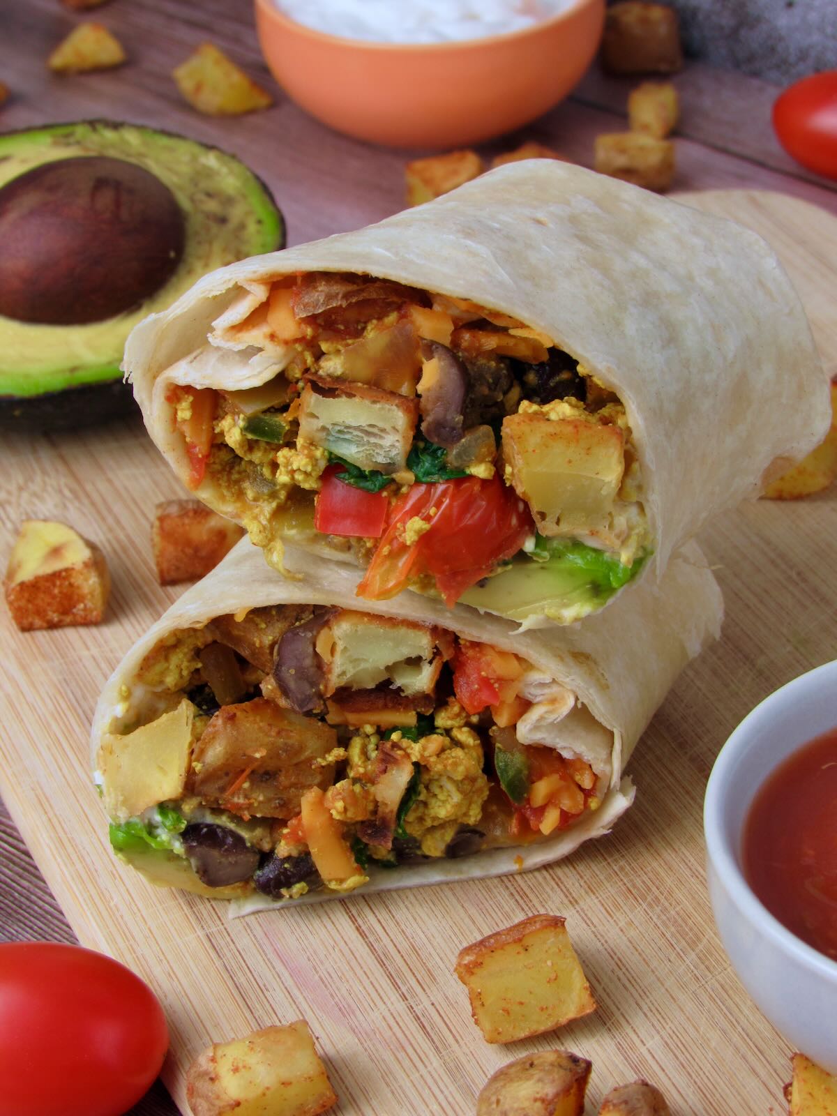 Vegan Breakfast Burrito sliced in half on a wooden cutting board to show roasted potatoes, tofu scramble, and veggie filling.