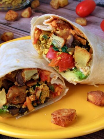 Two halved Tex Mex Vegan Breakfast Burritos with colorful vegetable filling on a yellow plate.