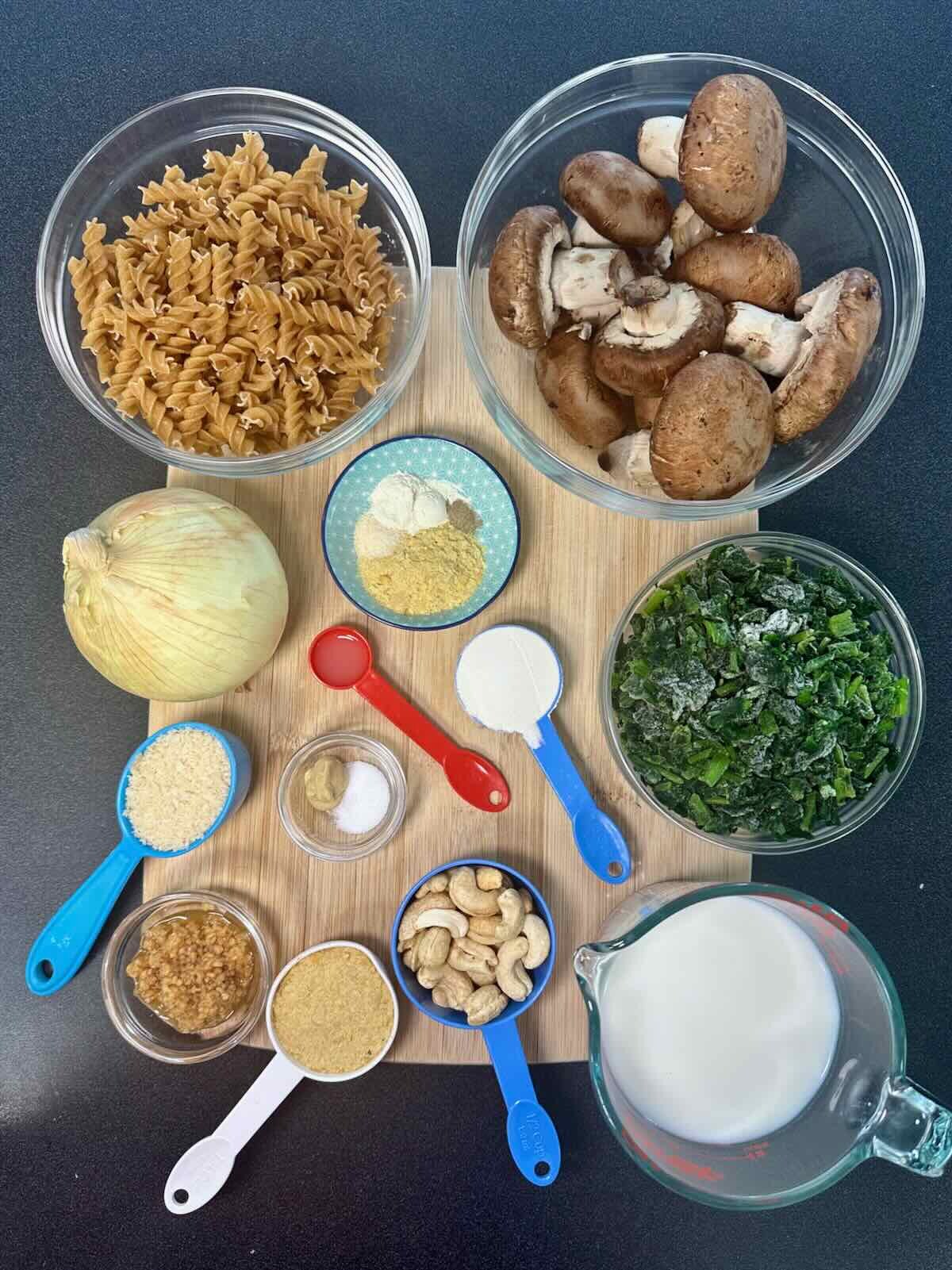 Overhead ingredients for Vegan Mushroom Spinach Pasta Bake on a bamboo cutting board.