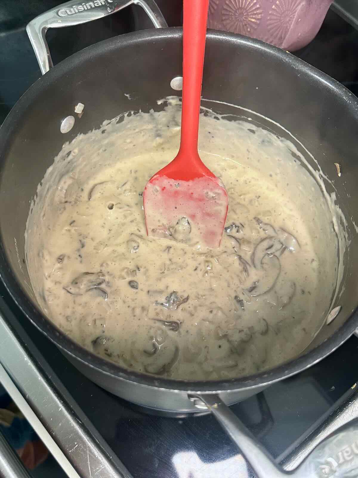 Creamy dairy-free mushroom sauce cooking in a pot with a red spatula.