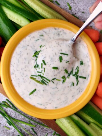 Easy Vegan Ranch Dressing in a yellow bowl, spoon lifted, with fresh vegetables around it.