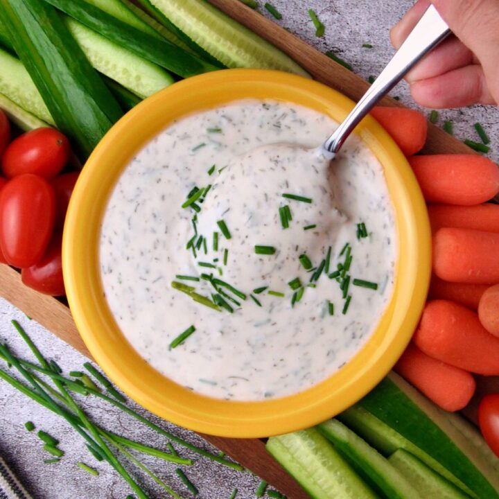 Easy Vegan Ranch Dressing in a yellow bowl, spoon lifted, with fresh vegetables around it.