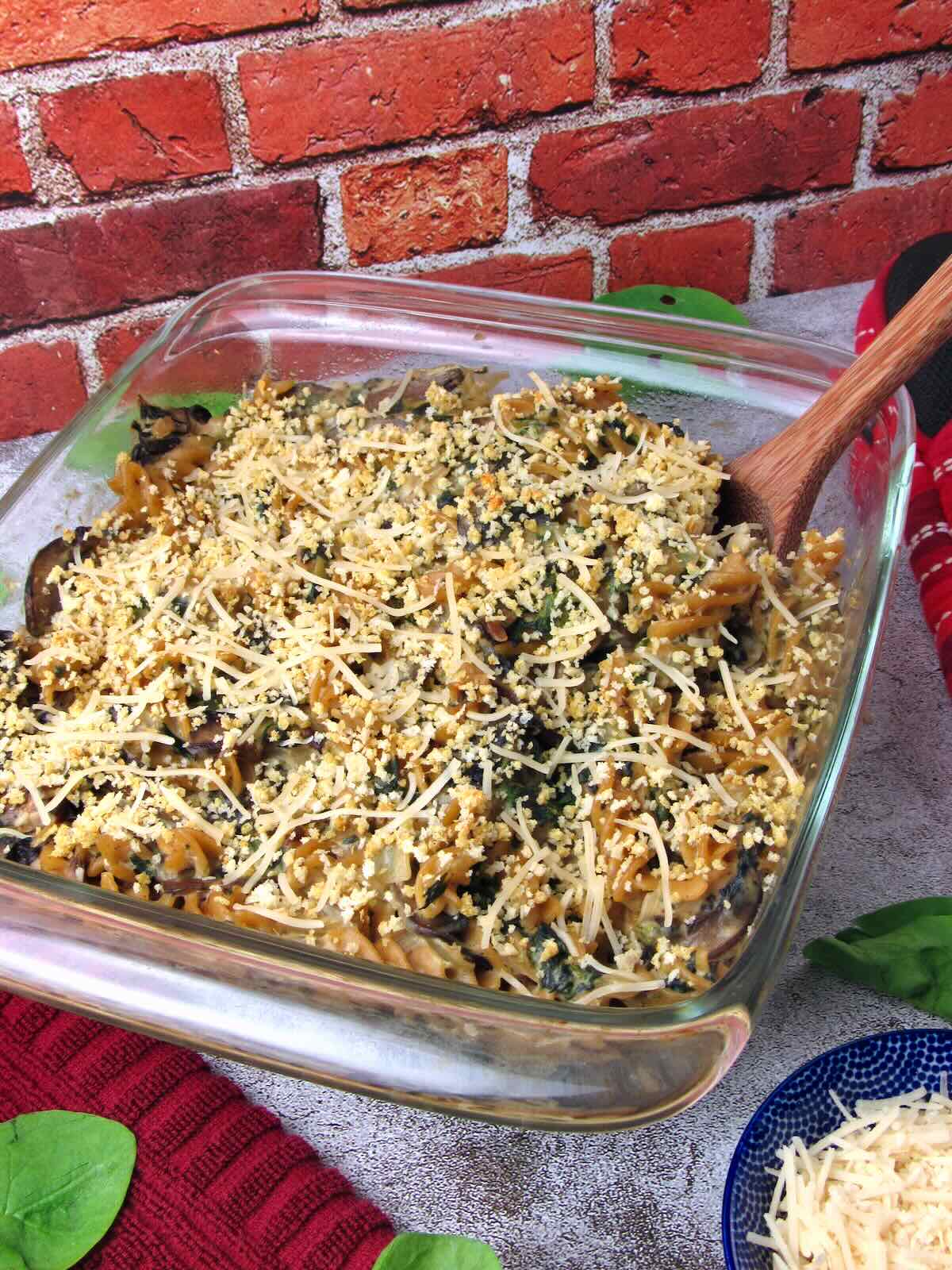 Baked Vegan Mushroom Spinach Pasta Casserole topped with crispy breadcrumbs and vegan parmesan in a clear glass dish.