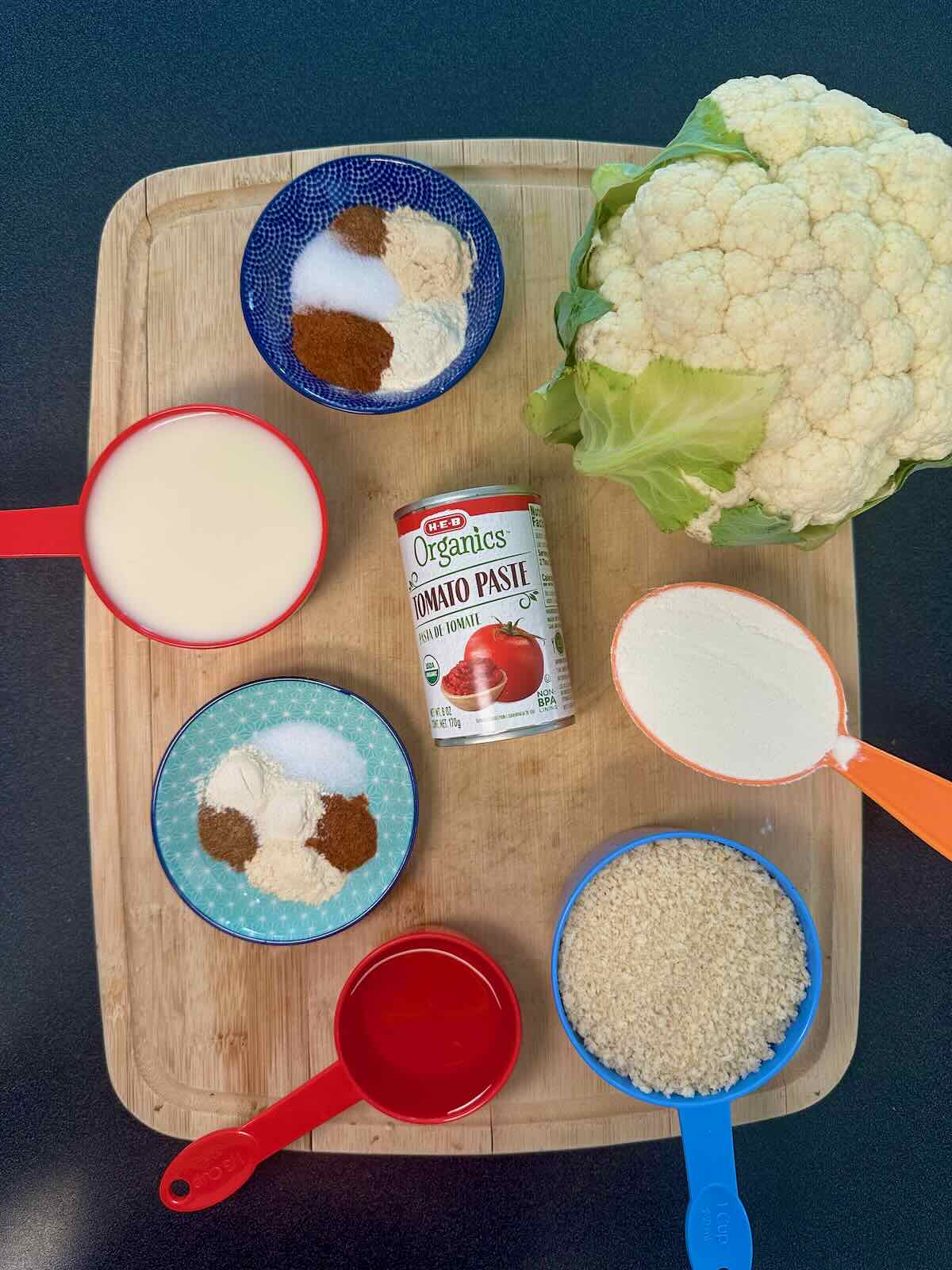 Overhead view of ingredients for Baked Buffalo Cauliflower, including cauliflower, tomato paste, bread crumbs, and spicy seasonings.