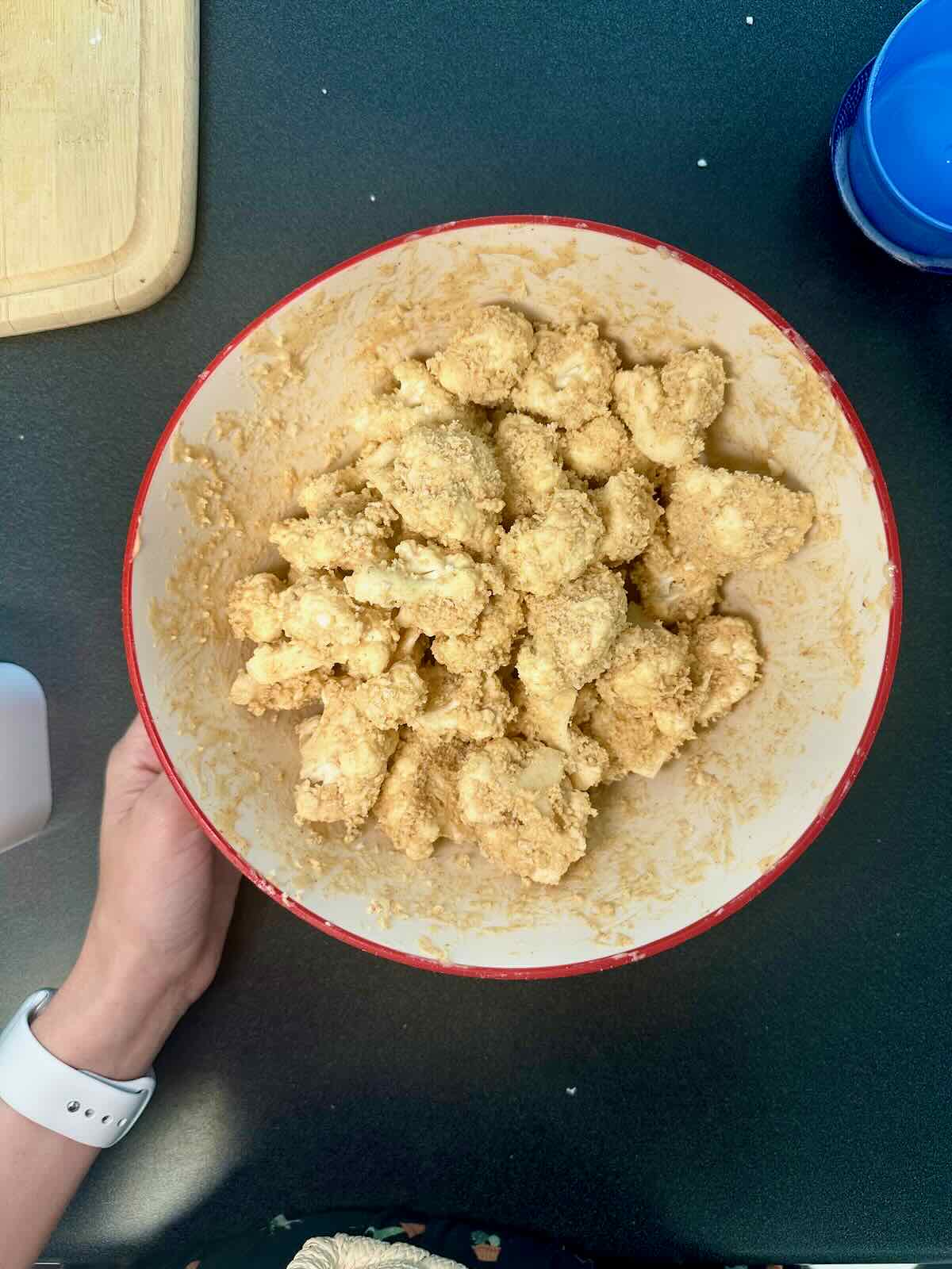 Coating cauliflower florets in batter and breadcrumbs for baking.