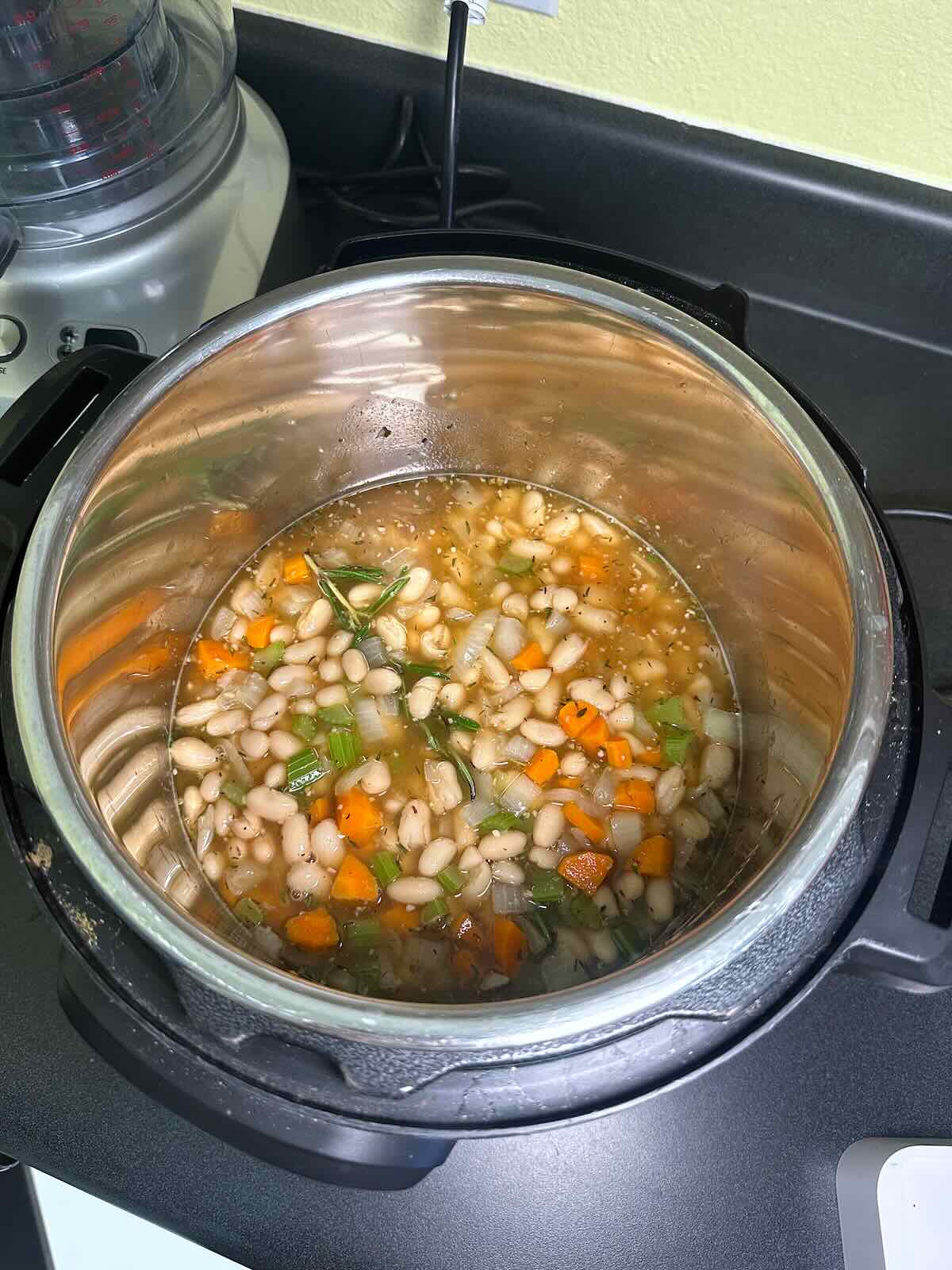 Adding broth, beans, and seasonings to Instant Pot soup. 