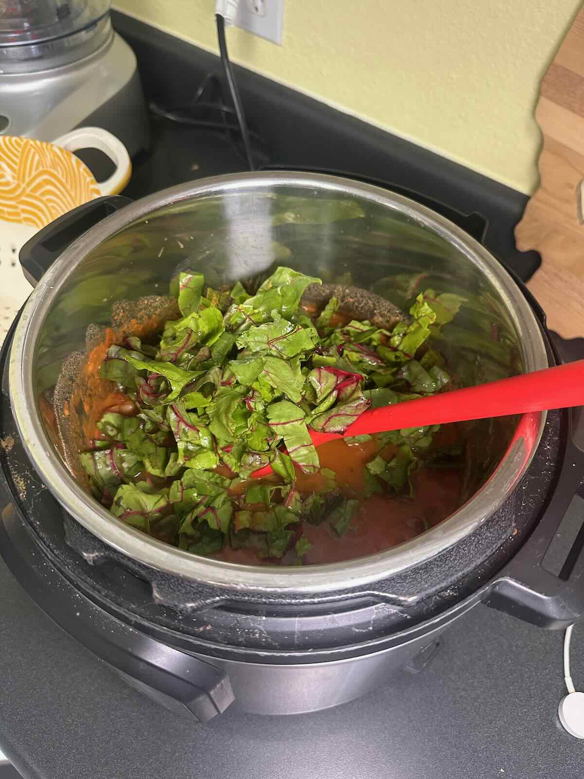 Mixing Swiss chard into White Bean Soup in the Instant Pot. 
