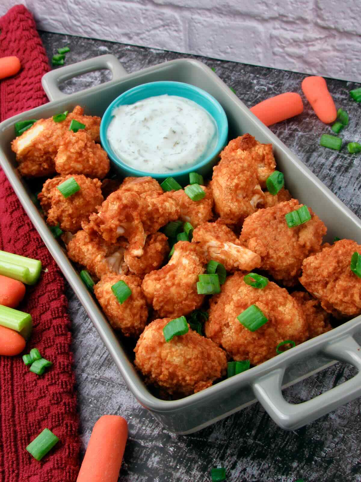 Platter of Crispy Buffalo Cauliflower Wings with Vegan Ranch Dressing and fresh vegetables.