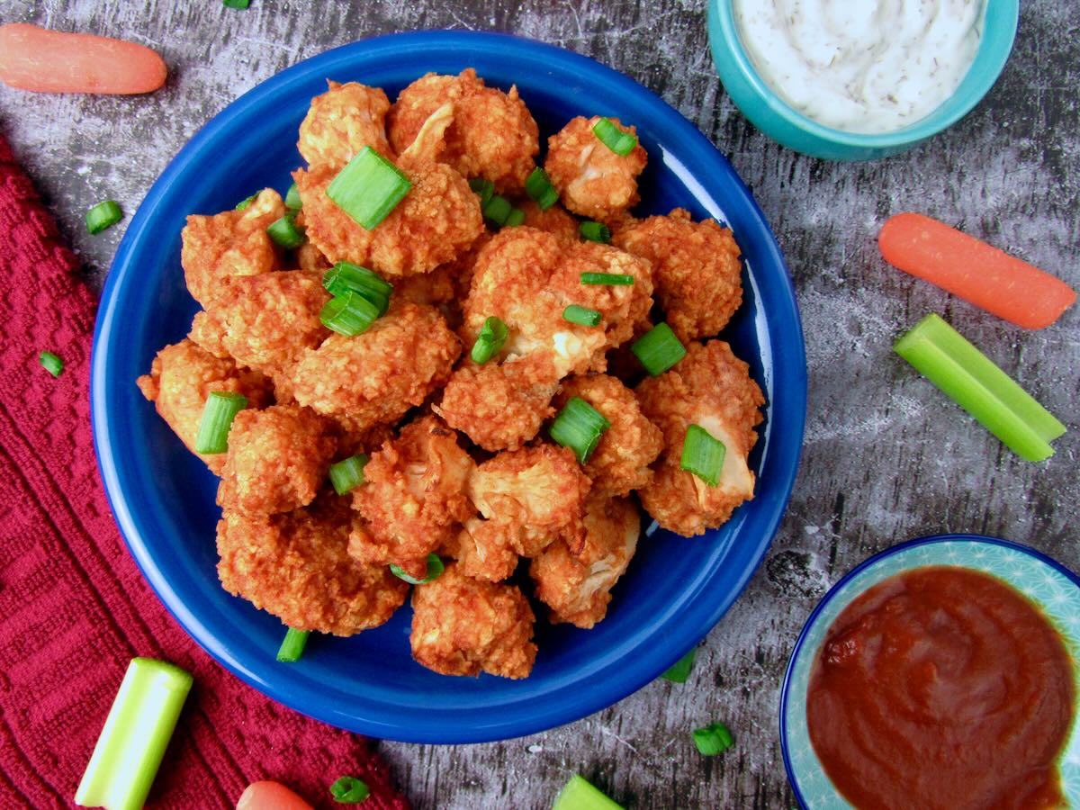 Blue plate of Oil-Free Buffalo Cauliflower Wings garnished with green onions, served with ranch and homemade buffalo-inspired sauce.
