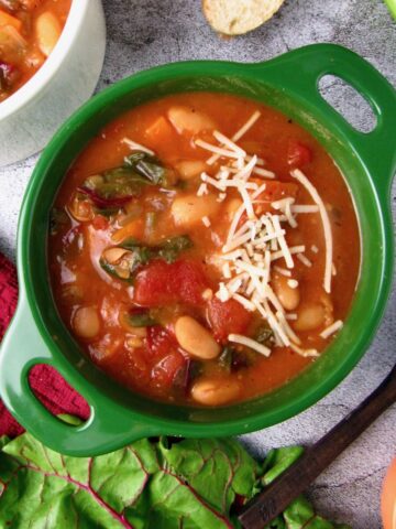 Vegan Instant Pot White Bean Soup with Swiss chard and tomatoes, topped with vegan parmesan.