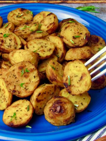 Crispy oil-free lemon roasted potatoes on a blue plate, garnished with fresh herbs.