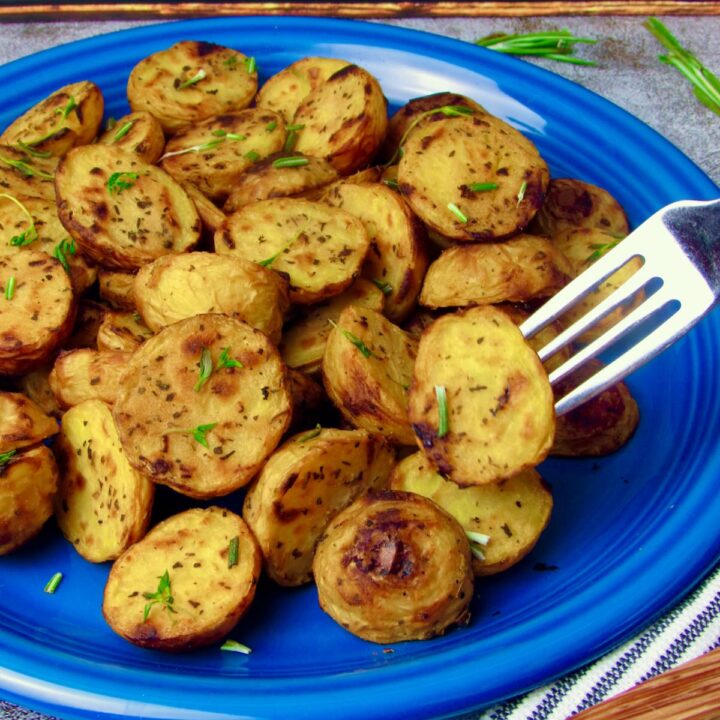 Crispy oil-free lemon roasted potatoes on a blue plate, garnished with fresh herbs.