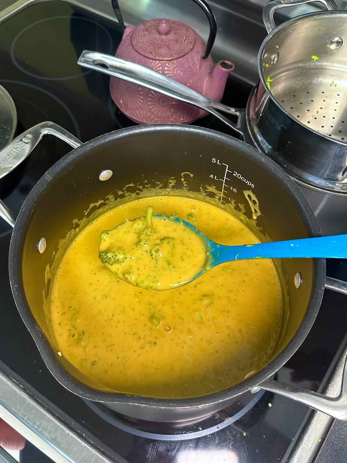Mixing steamed broccoli into a vegan cheddar soup.