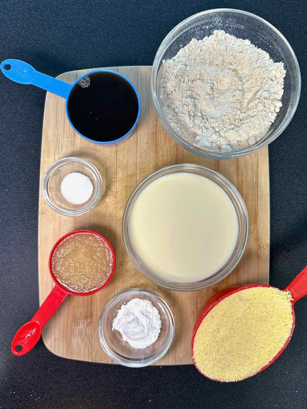 Overhead view of ingredients for vegan cornbread, including flour, cornmeal, baking powder, nondairy milk, applesauce, maple syrup, and salt.