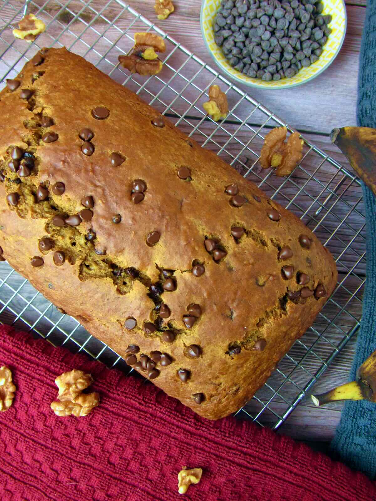 Overhead view of a Vegan Banana Bread loaf, surrounded by scattered walnuts and a bowl of vegan chocolate chips.