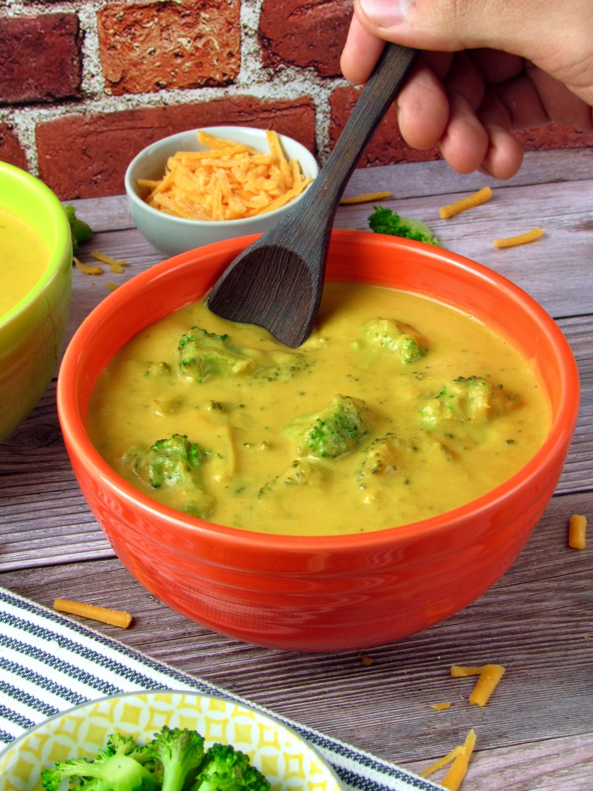 Vegan Broccoli Cheddar Soup, served in an orange bowl with a wooden spoon.