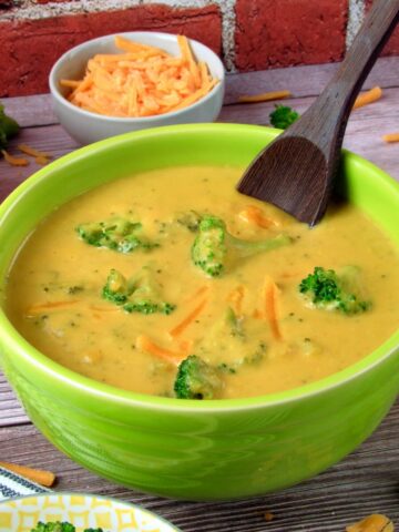 Creamy Vegan Broccoli Cheddar Soup in a green bowl, garnished with fresh broccoli florets and vegan cheddar cheese.
