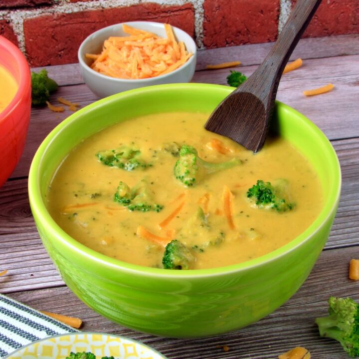 Creamy Vegan Broccoli Cheddar Soup in a green bowl, garnished with fresh broccoli florets and vegan cheddar cheese.