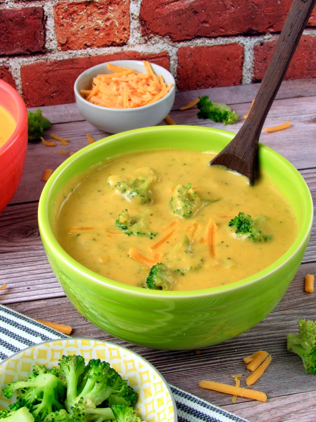 Homemade Vegan Broccoli Cheddar Soup, surrounded by fresh broccoli and shredded vegan cheddar.