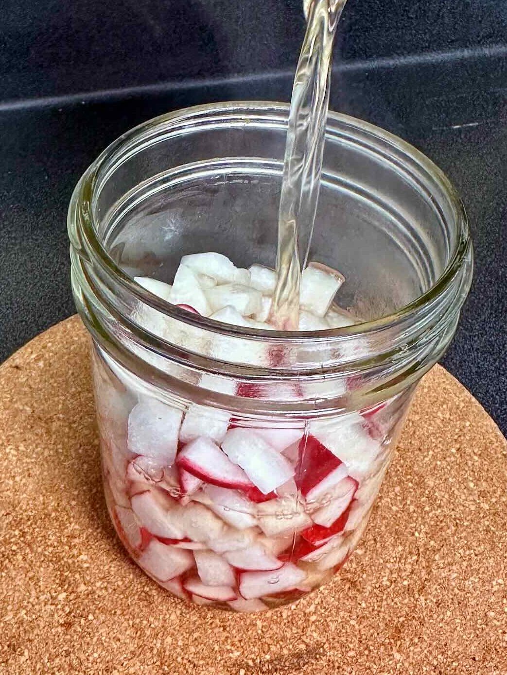 Pouring vinegar over radishes to created quick pickled radishes.