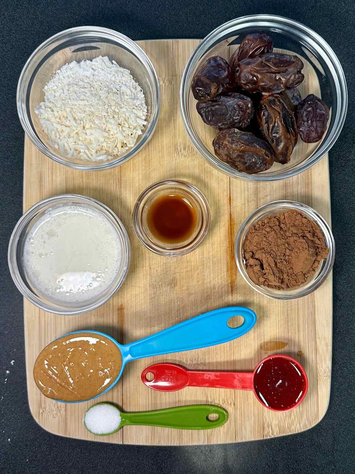 Overhead view of ingredients for vegan coconut date balls, including medjool dates, coconut milk, shredded coconut, natural peanut butter, and cocoa powder.
