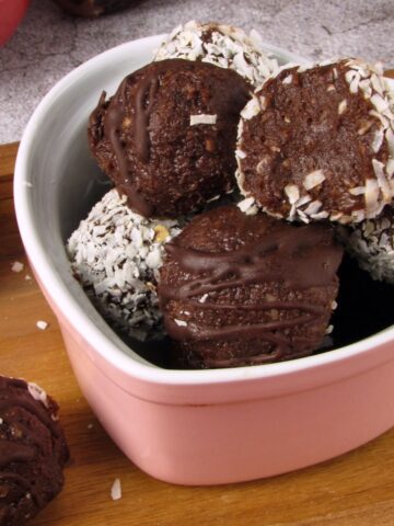 Chocolate coconut date truffle bites drizzled with chocolate and coated in shredded coconut in a pink bowl.
