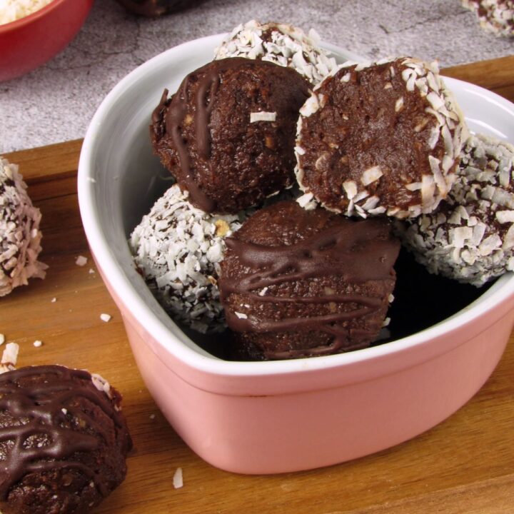 Chocolate coconut date truffle bites drizzled with chocolate and coated in shredded coconut in a pink bowl.