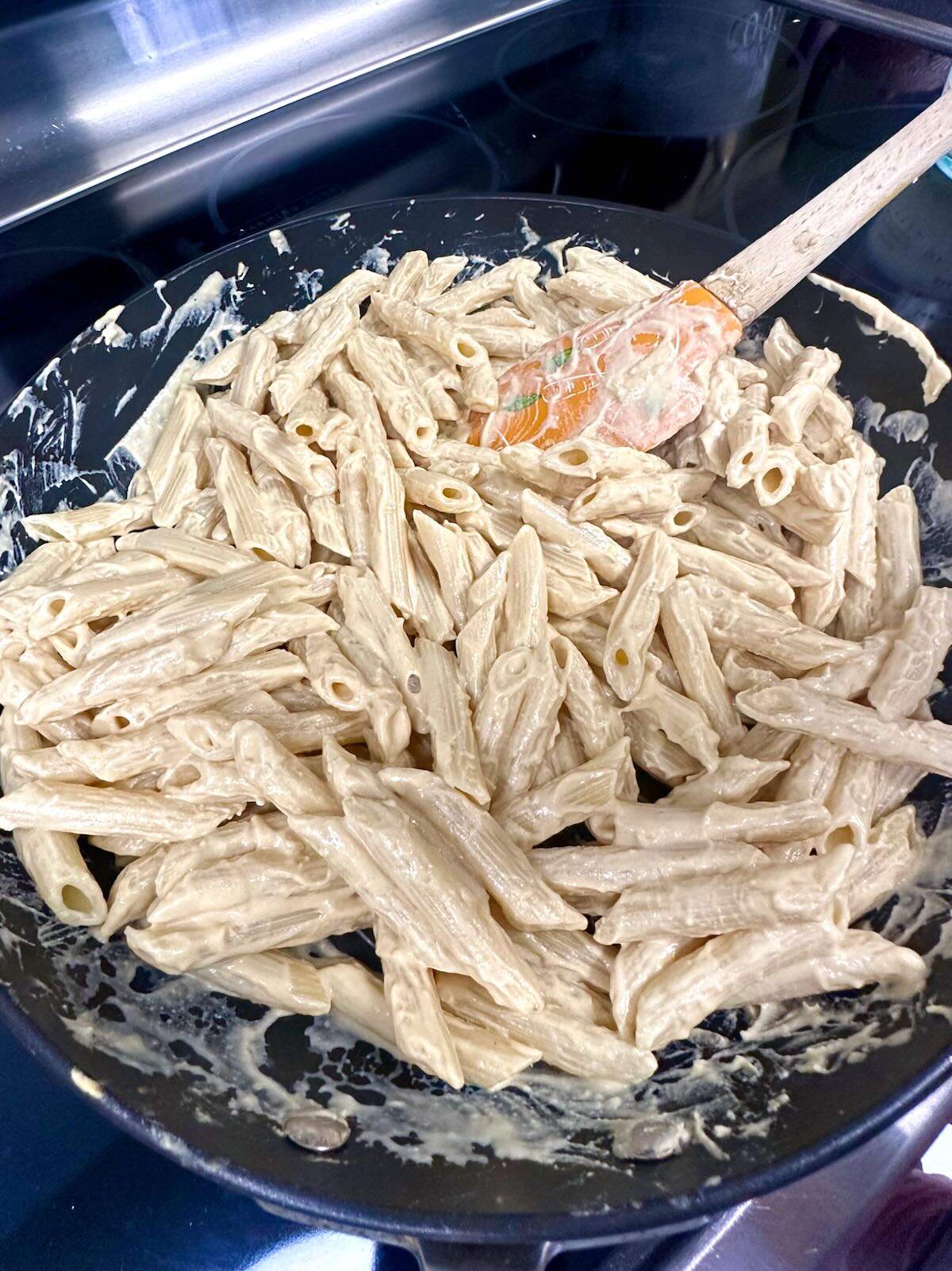 Mixing pasta and hummus pasta sauce.