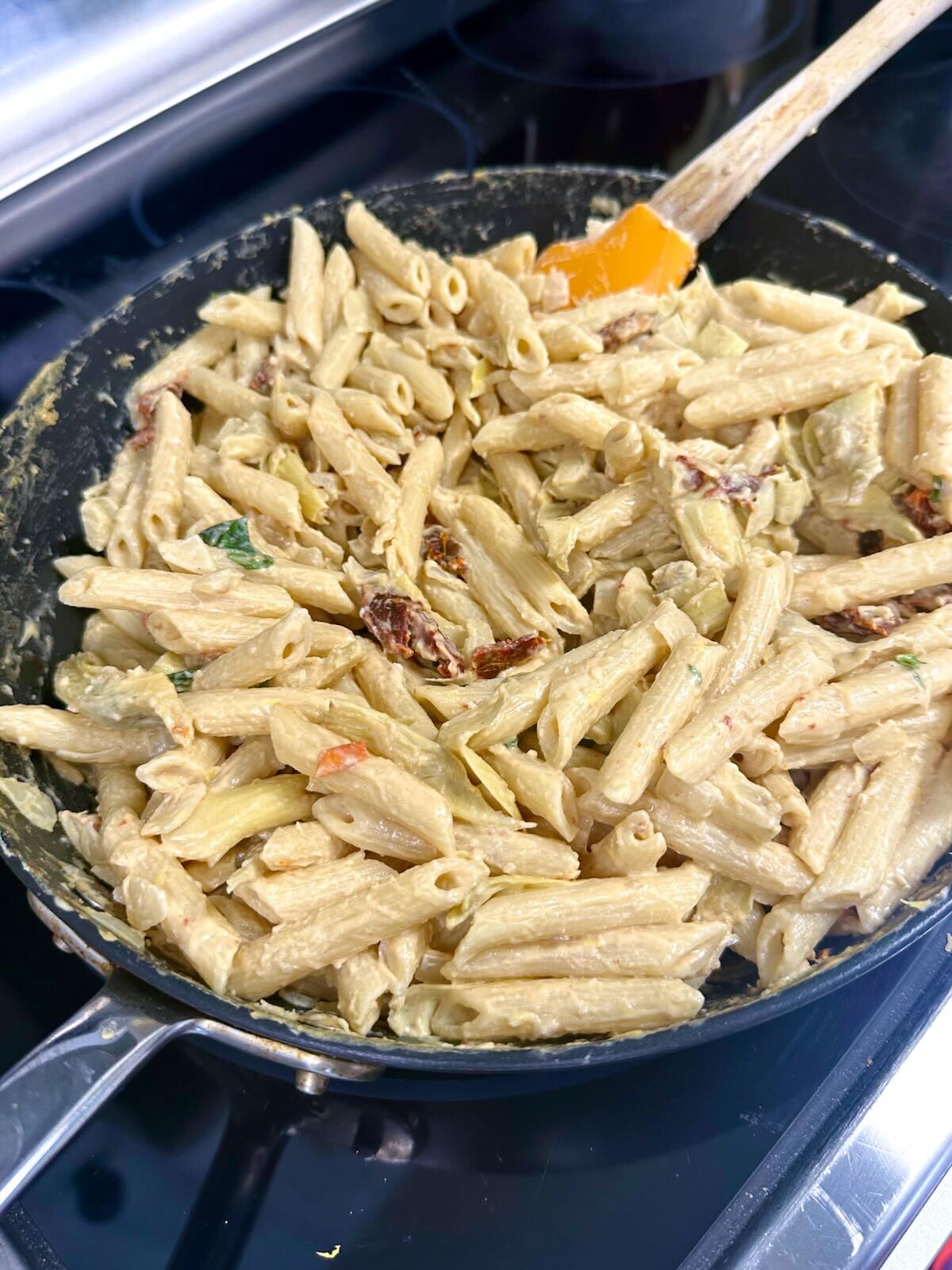 Mixing sun-dried tomatoes and basil into Vegan Artichoke Hummus Pasta.