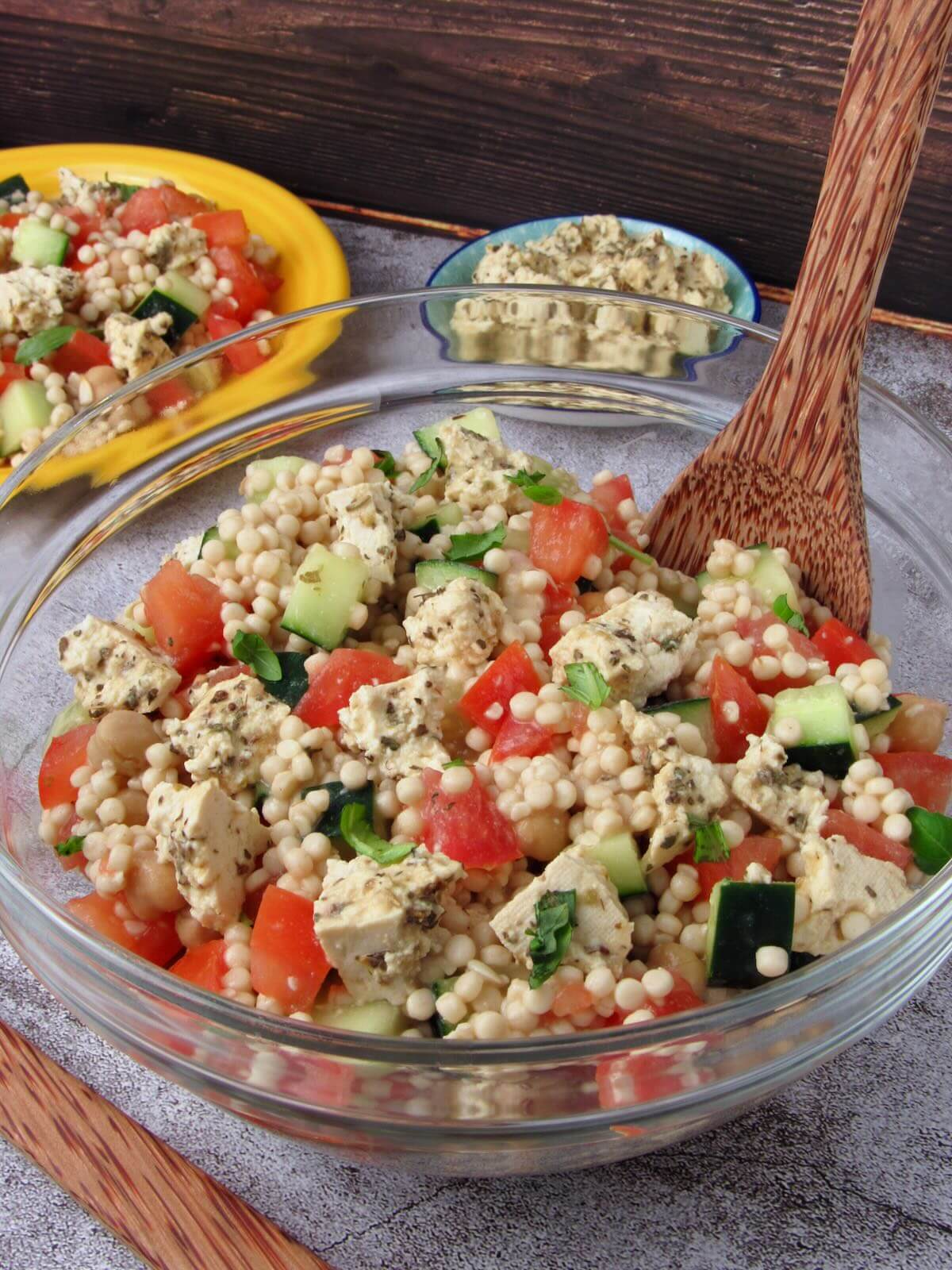 Israeli Couscous Salad in a bowl with tomato, cucumber, chickpeas, basil, and tofu feta.