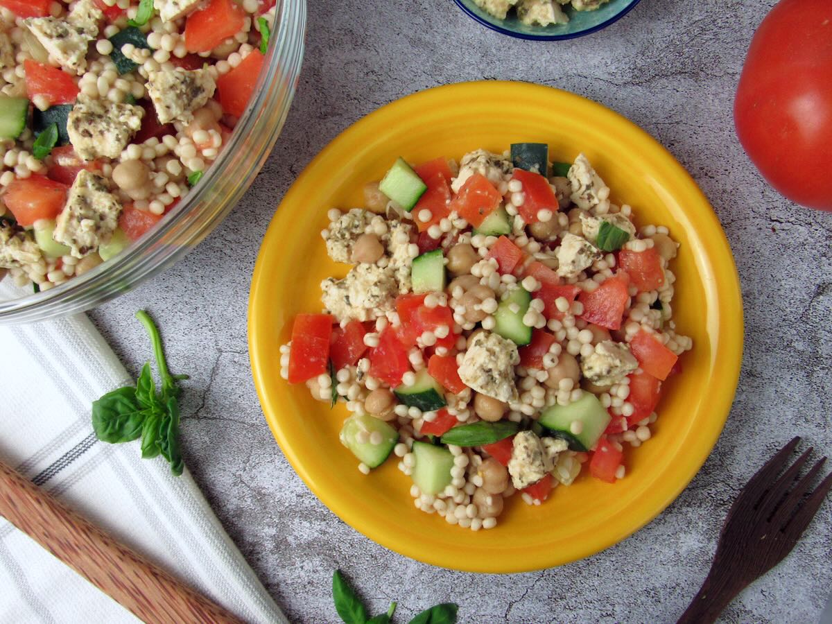 Pearl Couscous Salad served on a yellow plate with a tomato nearby.