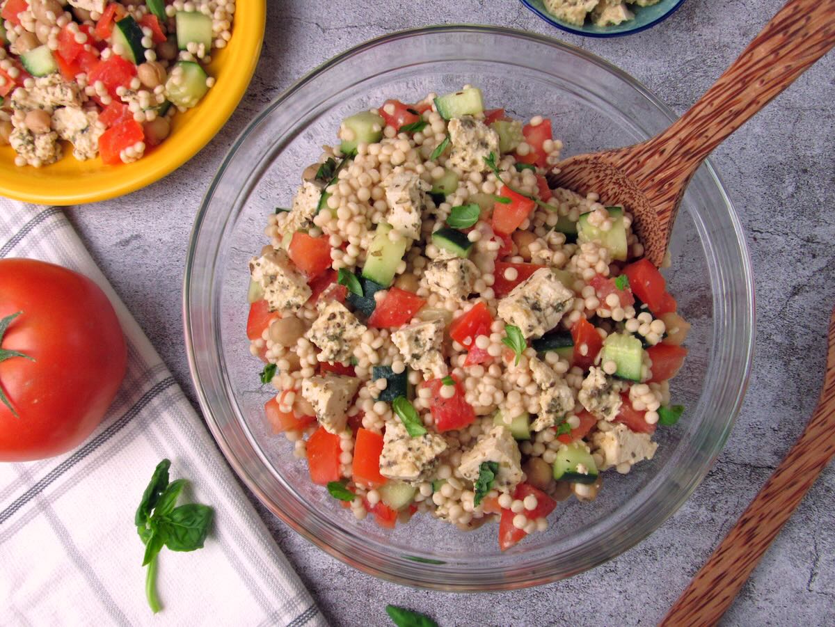 Large bowl of Couscous Salad with serving utensils and scattered basil.