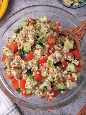Israeli couscous Chickpea Salad in a large bowl with tomato, cucumber, basil, and tofu feta.