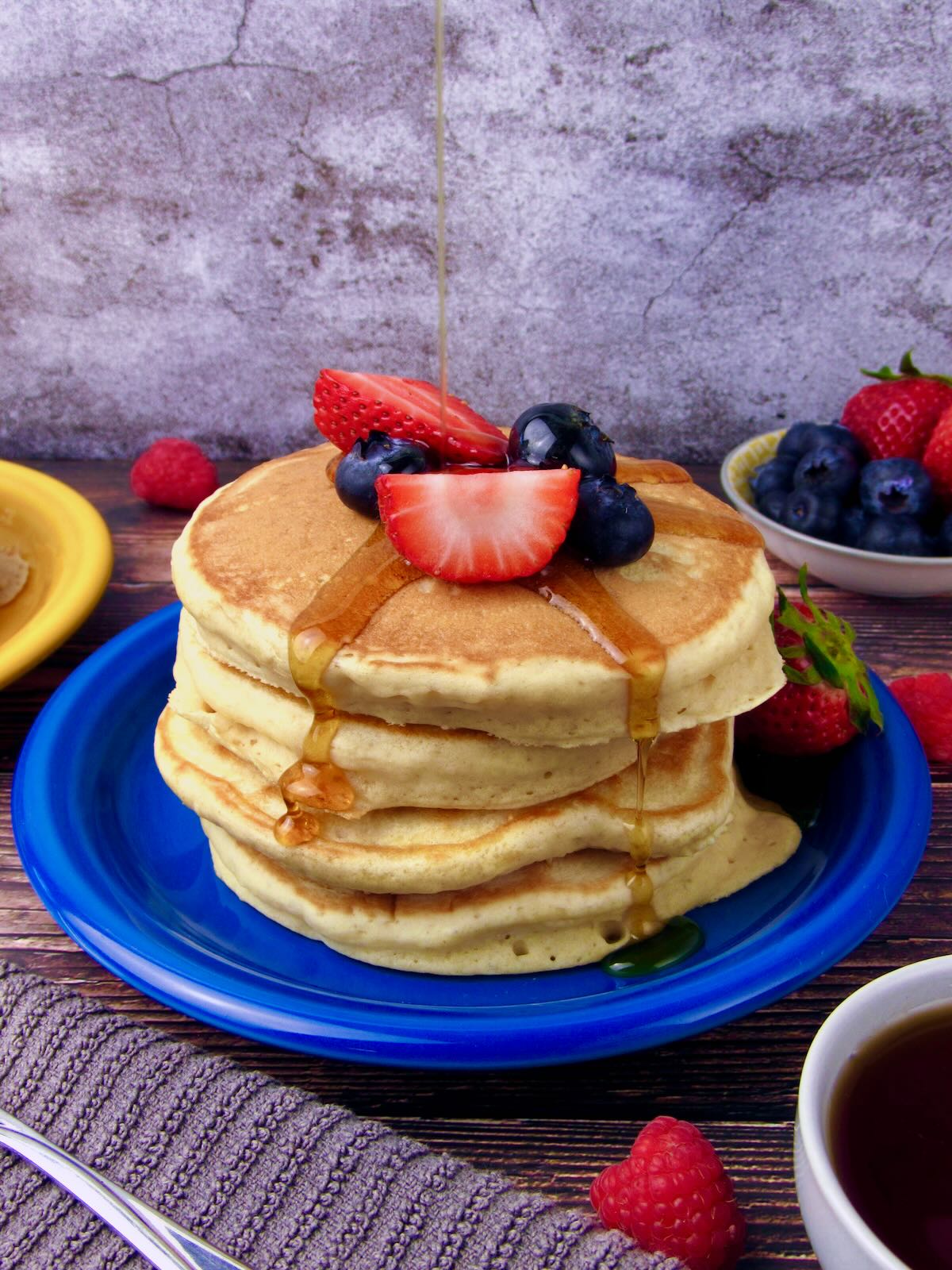 Stack of fluffy vegan buttermilk pancakes with maple syrup dripping down the sides, topped with fresh berries.