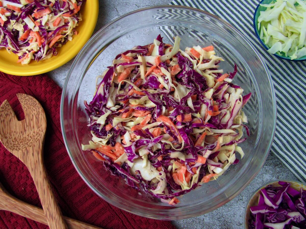 Large serving bowl of plant based coleslaw, with small bowls of cabbage surrounding it.