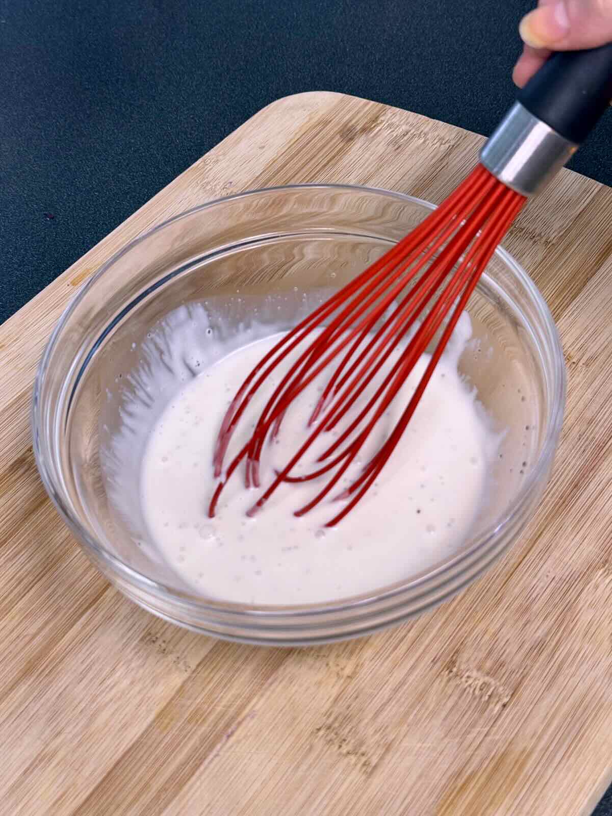 Vegan coleslaw dressing being whisked in a glass bowl.
