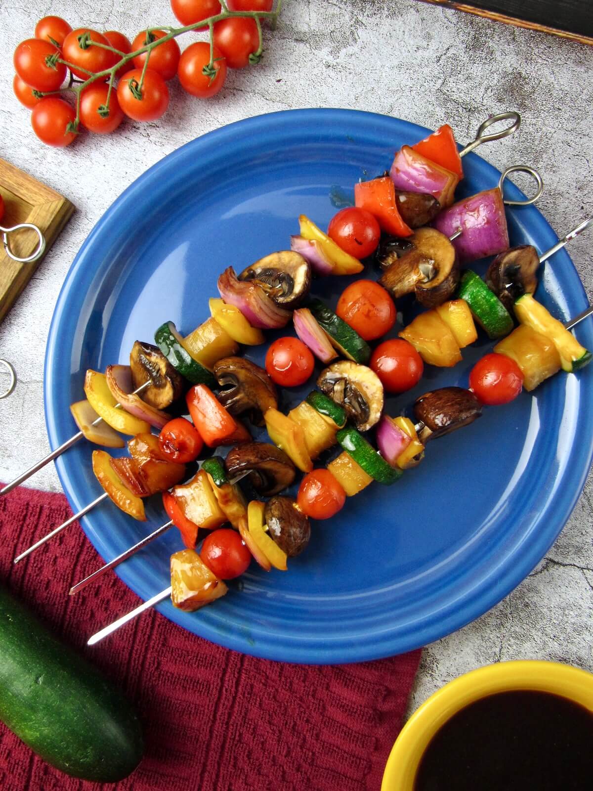 Pineapple Veggie Skewers on a blue plate, surrounded by cherry tomatoes, zucchini, and oil-free teriyaki sauce.